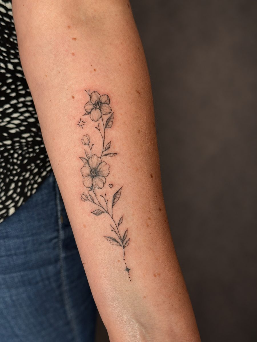 Fineline tattoo met een fijne botanische rank op de bovenarm, gezet in Lelystad