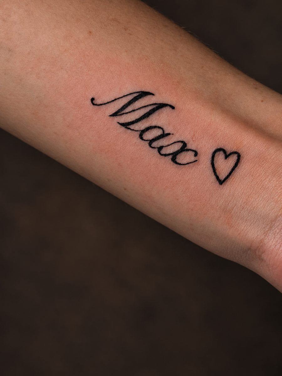 Fineline tattoo van een naam met een klein hartje op de onderarm, gezet bij EmmsTattoo in Lelystad