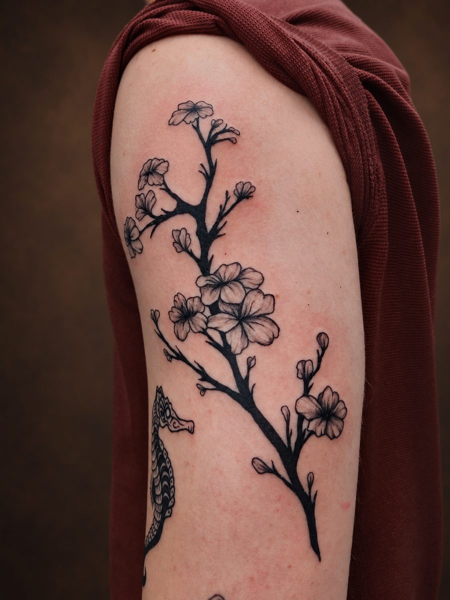 Floral tattoo van een kersenbloesemtak over schouder en bovenarm, gezet in Lelystad
